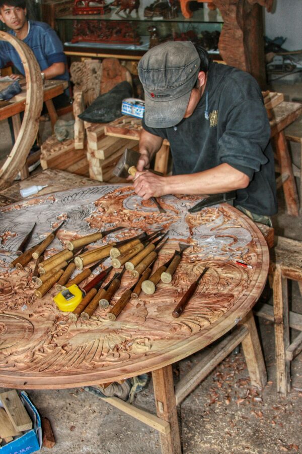 A craftsman intricately carving wood in a traditional Chinese workshop, highlighting skilled craftsmanship.